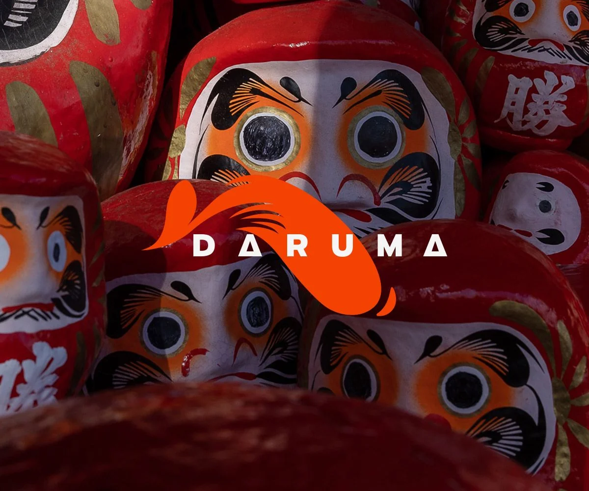 Rows of red daruma dolls, with the Daruma wordmark and its orange eyebrow isotype over them.